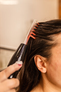 Woman combing hair with electric comb. d'Arsonval is a device for the physiotherapeutic effect on the tissues of the human body with a high-frequency, high-voltage and low-current impulse quick