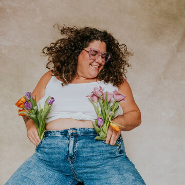 Plus size women with glasses wearing jeans and a white shirt holding tulips