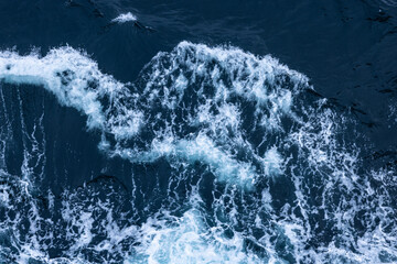 Looking down at the surface of dark deep Atlantic Ocean white foamy wake waves coming from cruising...