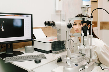 Ophthalmologist with slit lamp examines eyes and cornea of woman. Ophthalmologist illuminates eye...