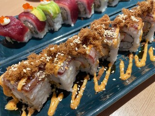 A close-up, top-down view showcases two rows of beautifully crafted sushi rolls on a textured blue plate.