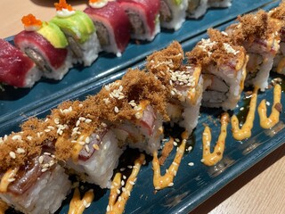 A close-up, top-down view showcases two rows of beautifully crafted sushi rolls on a textured blue plate.