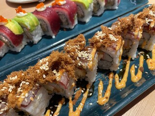 A close-up, top-down view showcases two rows of beautifully crafted sushi rolls on a textured blue plate.