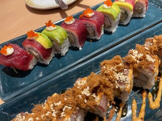 A close-up, top-down view showcases two rows of beautifully crafted sushi rolls on a textured blue plate.