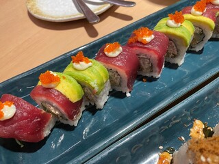 A close-up, top-down view showcases two rows of beautifully crafted sushi rolls on a textured blue plate.