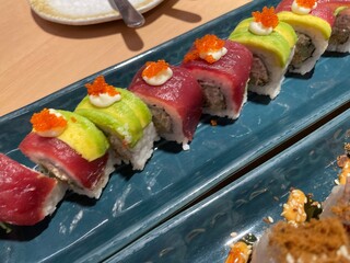 A close-up, top-down view showcases two rows of beautifully crafted sushi rolls on a textured blue plate.