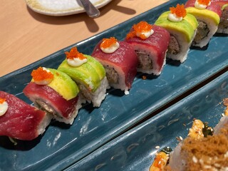 A close-up, top-down view showcases two rows of beautifully crafted sushi rolls on a textured blue plate.