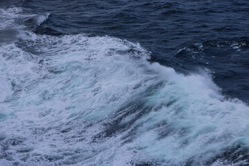 Photo of ocean wavy surface white foam wake coming from sailing cruise ship.