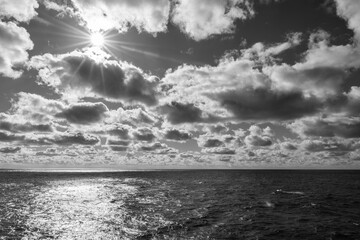 Black and White photograph of alluring ocean horizon appealing cloudscape and sun rays reflecting...