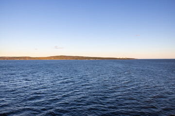 Photograph of Calm rippling ocean water surface land on the horizon on bright blue sunny morning.