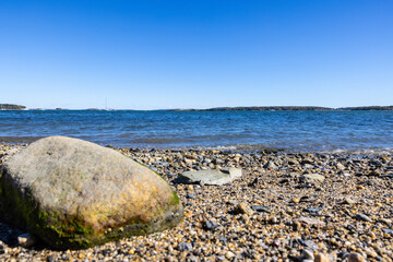 Photograph of one large boulder rock on a pebble beach shore deep blue calm ocean water.