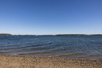 Photograph of pebble sandy shore with calm rippling waters on bright blue clear day