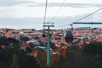 Cable car descending toward Funchal, Madeira, with panoramic views of the city terracotta rooftops,...