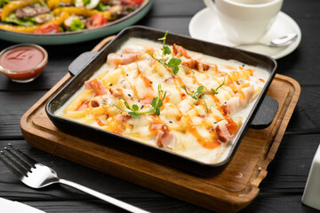 A hot pan of baked potatoes with meat and bacon in a creamy sauce is served at a restaurant on the table