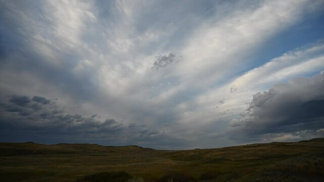 Time lapse of radiating summer clouds moving above rolling dry prairie grass and hills
