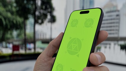 GREEN SCREEN CHROMA KEY Smartphone with a green screen held outdoors in a modern urban setting with high-rise buildings and traffic in the background
