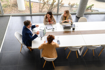 High angle view of business professionals with technologies and documents reviewing project details...