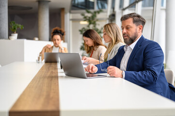 Male professional holding glasses and using laptop while female colleagues working together in meeting