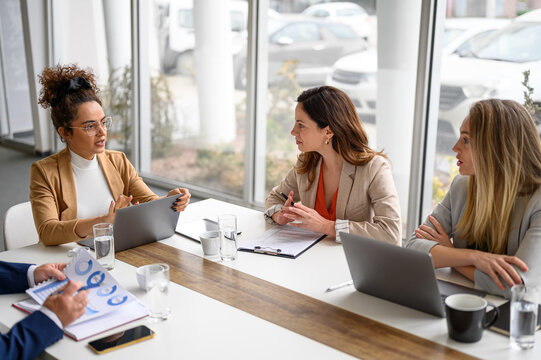 Female professionals exchanging ideas and strategies with laptop and document on table in board room