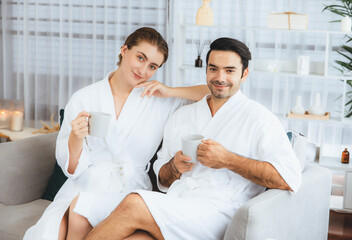 Obraz premium Beauty or body treatment spa salon vacation lifestyle concept with couple wearing bathrobe relaxing with drinks in luxurious hotel spa or resort room. Vacation and leisure relaxation. Quiescent