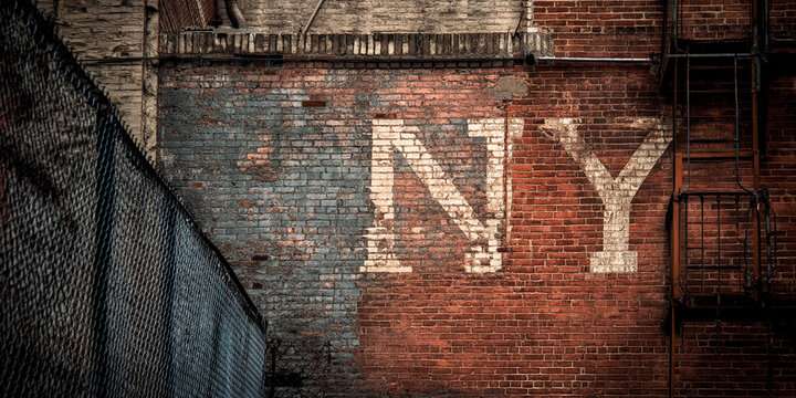 Brick wall texture with faded "NY" lettering, showcasing urban decay and history, representing city life, nostalgia, and aged aesthetics