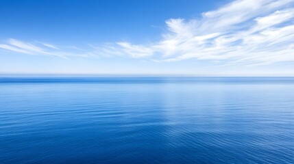 Obraz premium Calm blue ocean water meets the horizon under a bright blue sky with clouds.