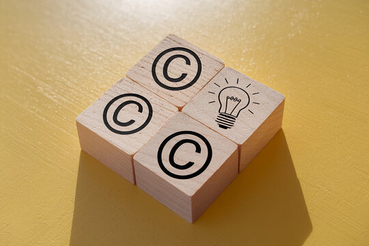 Three wooden cubes display copyright symbols, one shows a lightbulb, symbolizing intellectual property and creative ideas, perfect for business or legal concepts