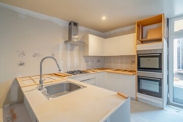 In a contemporary kitchen, renovation activities unfold with uninstalled cabinets and new appliances. Natural light streams through the large window, enhancing the unfinished space feel