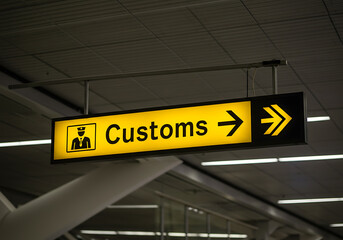 A lit-up customs sign with an arrow, guiding travelers towards the customs area at an airport.