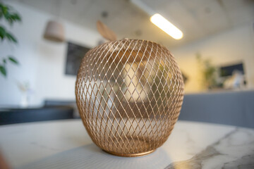 A copper wire apple-shaped object, possibly a napkin holder or vase, is placed on a white marble...