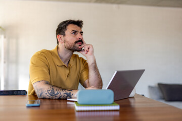 Freelancer is sitting at his desk, looking away with hand on chin, thinking and working on his...