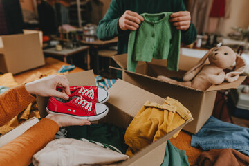 Unrecognizable man and woman putting an old out-of-use kid clothes and shoes in boxes for charity