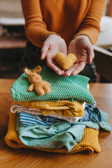 Close-up of female hands holding a fabric heart near kid clothes and toys for charity