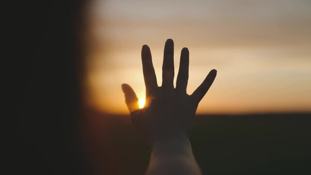 Reaching out to the sun, happy girl at sunset, sunlight shining on her hand, solar system star, happy family concept, touching a dream, asking for help from God, natural phenomenon.