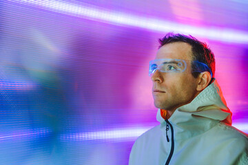 Futuristic portrait of man using glowing virtual reality glasses standing in front of neon lights...