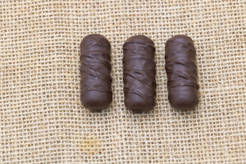 Three chocolate pralines shaped like elongated cylinders on a fabric background