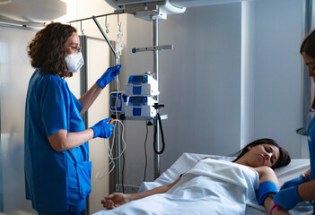 Nurse preparing infusion pump for patient lying in hospital bed