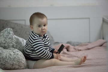 Toddler boy holding remote on bed