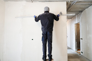 A construction worker plasters a concrete wall with a rule, skillfully leveling the surface to obtain an impeccable finish as part of a renovation project. High quality photo