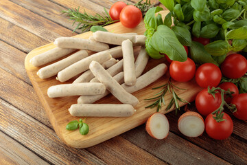 Bavarian white sausages with basil and tomatoes on a cutting board.