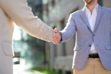 Close-up of a handshake between a man and a woman in business attire outdoors. Symbol of agreement,...
