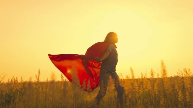 a girl plays a superhero at sunset, red cape costume on running child, childhood dream of saving the weak, teenager kid wants to be strong saving world, children traveler runs in sun, festive fun day.