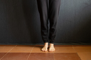 A barefoot young girl in a black tracksuit stands near the wall