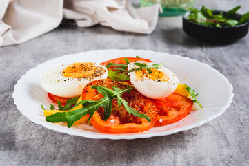 Light appetizer of tomatoes, boiled egg, cheese and arugula on a plate on the table