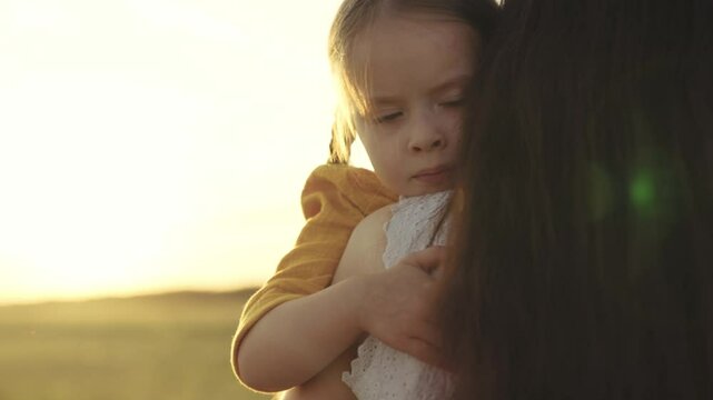 little kid hugs mother in the rays of the sun, happy family at sunset, woman loves child, take motherhood a pleasant feeling, girl daughter with mom on a journey against the sky, custody of baby.