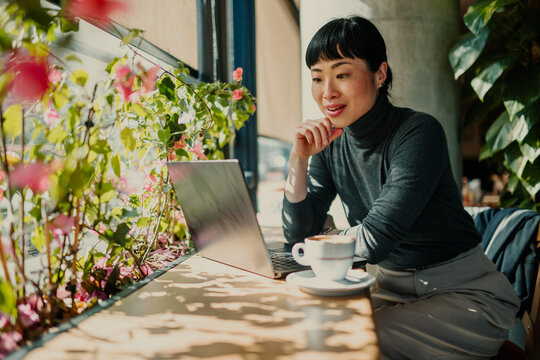 Asian freelancer working on laptop in cafe with plants