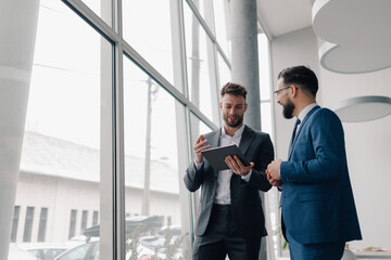 Two businessmen discussing work using tablet in modern office by window