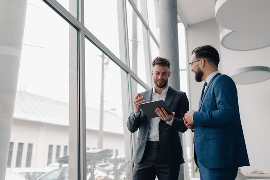 Two businessmen discussing work using tablet in modern office by window