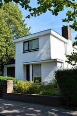 Modern white house situated in a green neighborhood with large windows and neat landscaping, bathed in sunlight on a clear day