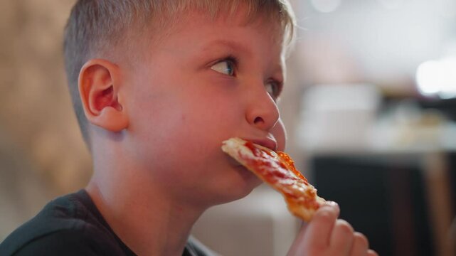 close up of young boy eating grilled pepperoni pizza slice indoors with cheeks puffed out enjoying cheesy slice casual mealtime setting blurred soft background